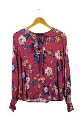 Blusa rosada con flores azules y blancas, manga larga con pretina en puño, cuello v con amarre. Busto: 100 cm. Largo: 60 cm.